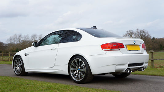 White BMW E9X M3 coupe in driver-side profile view showing its low stance and factory wheels