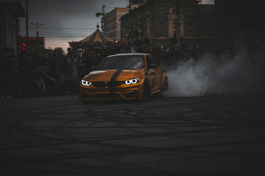 Orange BMW M3 drifting on a road with tire smoke