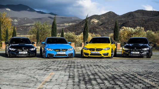 Four BMW F80 M3 sedans in black, blue, yellow, and black lined up nose-in on a mountain overlook