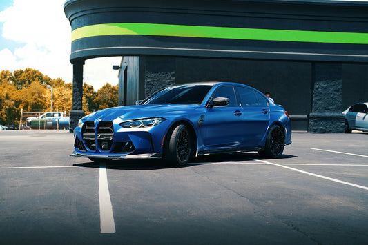 Blue 2025 BMW G80 M3 parked outdoors, rear three-quarter view showing quad exhaust and rear diffuser